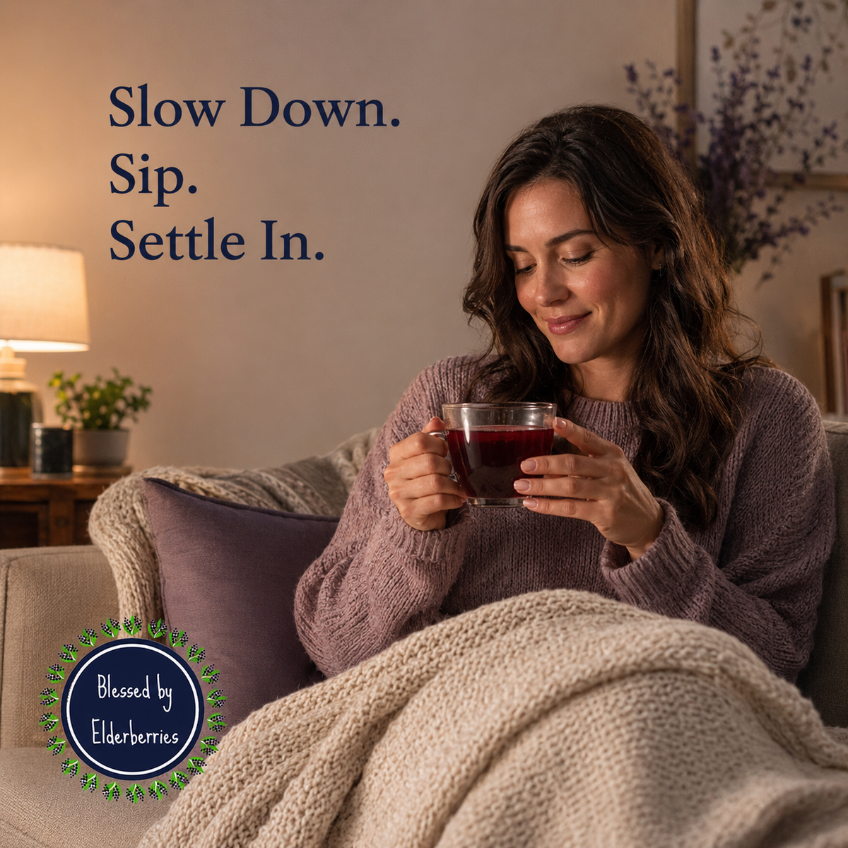 Woman relaxing under a blanket with a clear glass cup of dark ruby Soothe elderberry tea