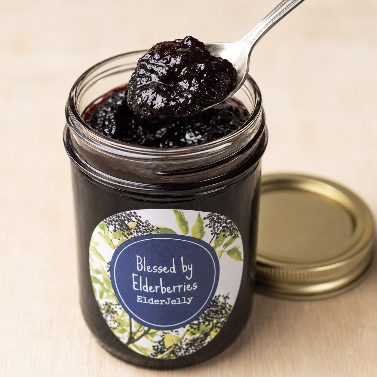 Open jar of Blessed by Elderberries Elderberry Jelly with a spoonful showing its thick, dark purple texture